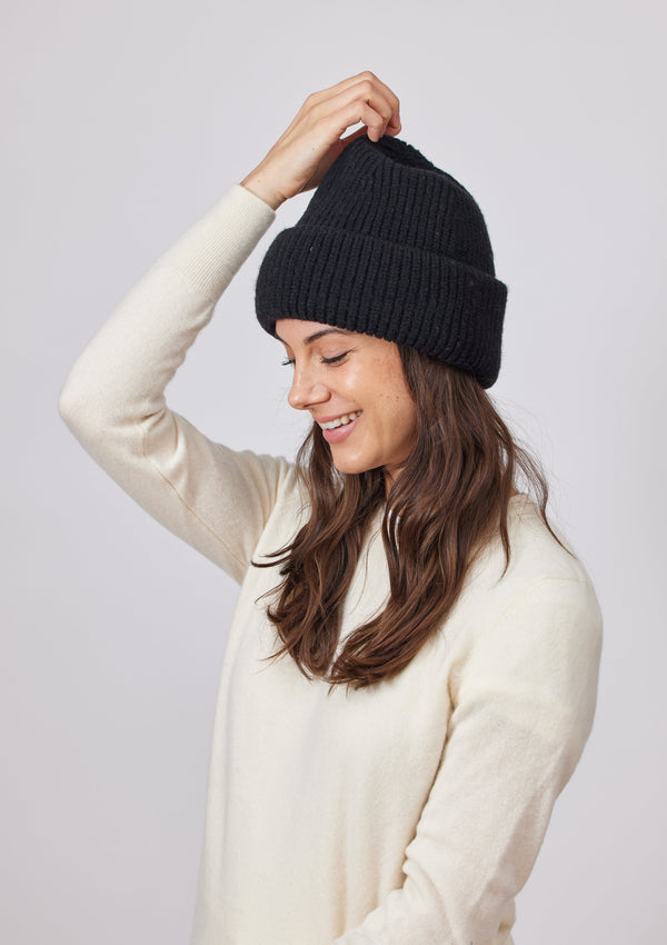 Model wearing black knit cuffed beanie and holding head