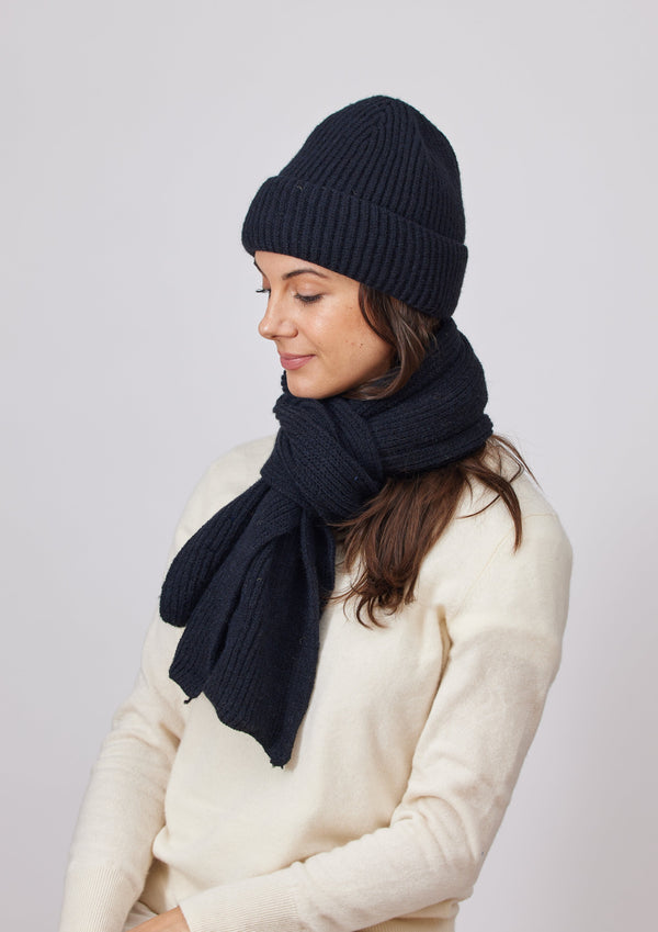 Model looking to her right and wearing a black ribbed knit beanie and scarf
