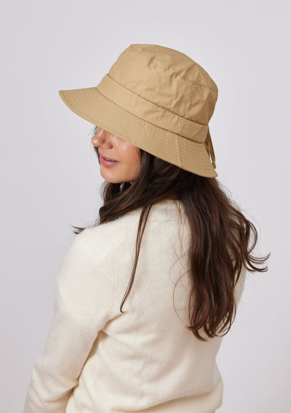 Model wearing a camel brown water resistant bucket hat and ivory sweater