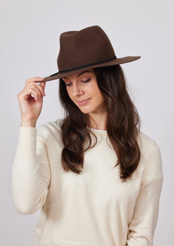 Model wearing a brown wool felt brimmed hat and holding brim