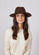 Model looking right and wearing brown wool felt brimmed hat and cream sweater