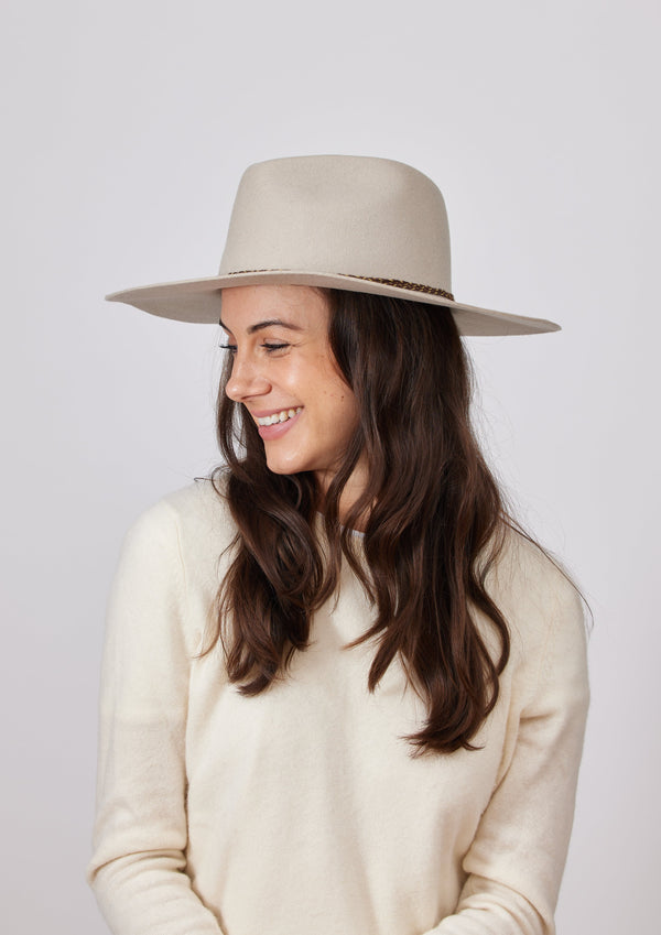Model looking to her right and wearing beige felt brimmed hat with brown chain trim detail