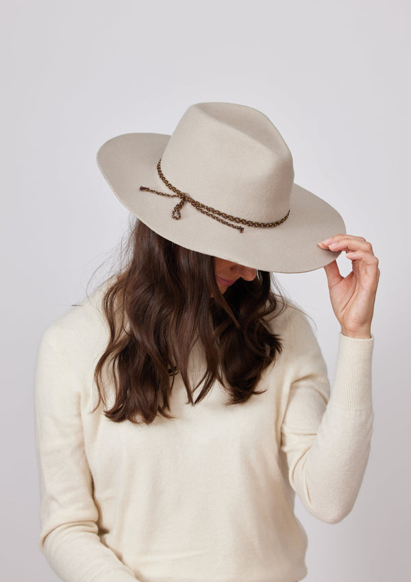 Model wearing beige felt brimmed hat with brown chain trim detail