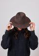 Model holding brim of brown velour brimmed hat