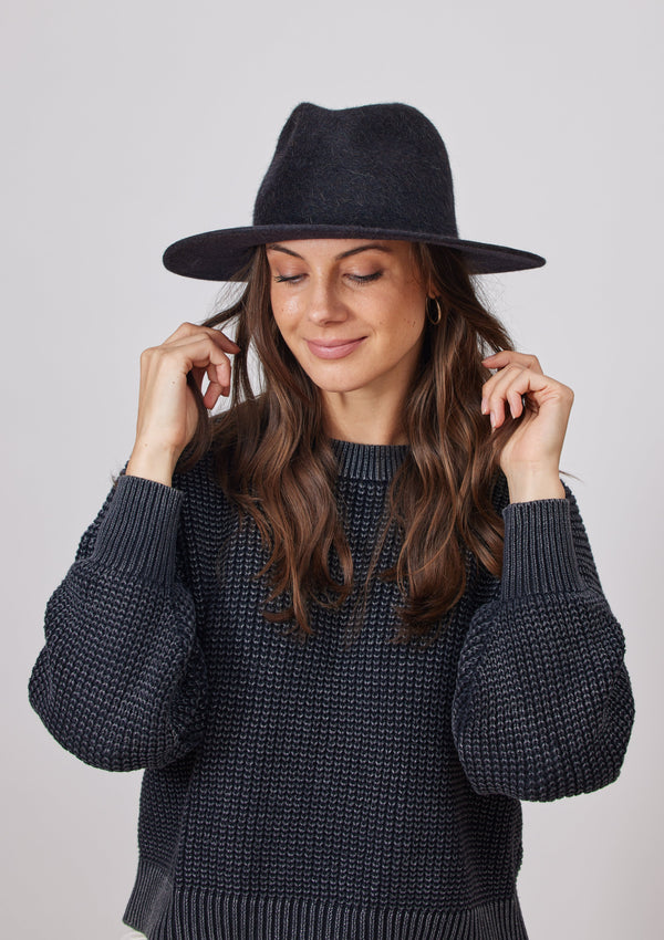 Model wearing black velour brimmed hat and playing with hair