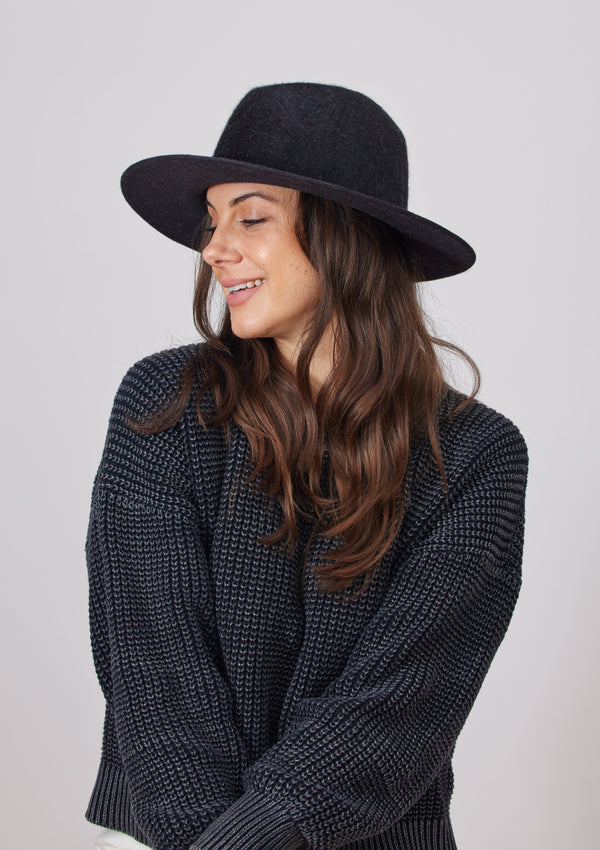 Model wearing black velour brimmed hat and smiling to her right