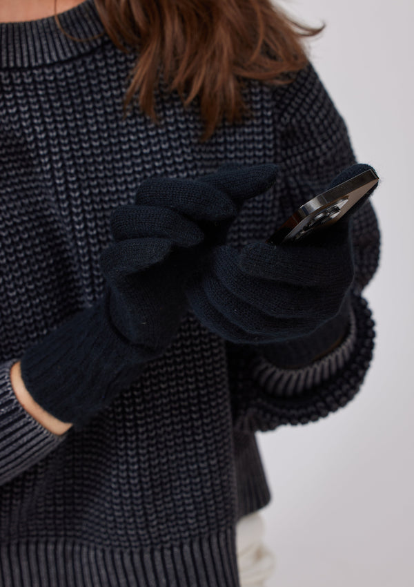 Model wearing grey sweater and black cashmere texting gloves with phone in her hand