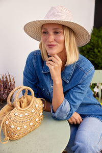 model sitting at a table, wearing a straw hat and small straw bag