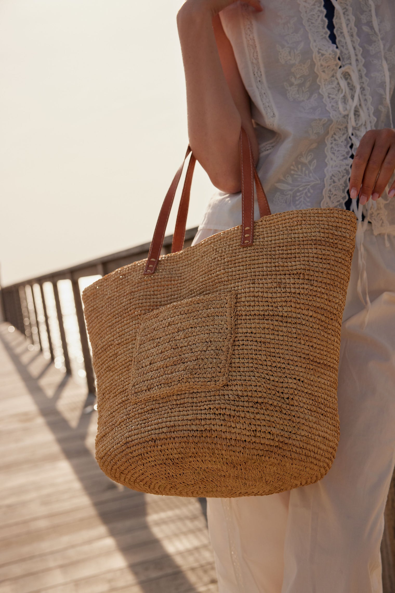Close up of model wearing straw tote with a pocket on the outside