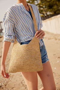Model holding a straw crossbody bag and wearing a striped shirt