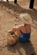 Model sitting at beach and wearing a brimmed panama hat