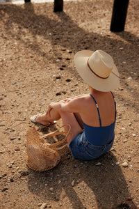 Model sitting at beach and wearing a brimmed panama hat