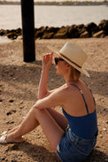Model holding brim of panama hat while sitting on beach