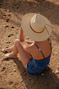Model wearing blue swimsuit and brimmed panama straw hat