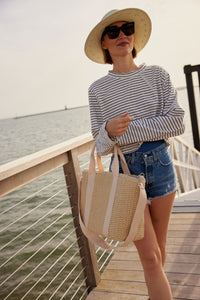 Model holding a straw cooler tote while standing on a pier
