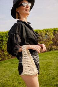 Model holding light tan cotton mini bag and black outfit
