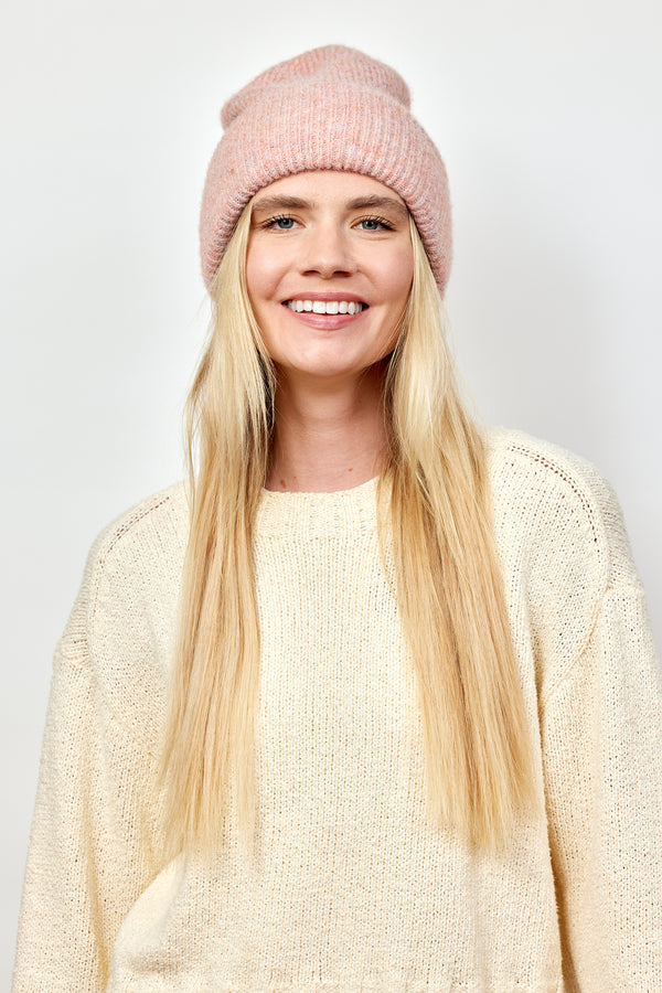 Model smiling while wearing light pink cuff beanie