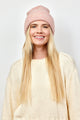 Model smiling while wearing light pink cuff beanie