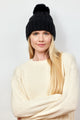 Model crossing her arms and wearing black cable knit beanie with pom