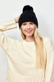 Black cable knit beanie with pom on model wearing ivory sweater