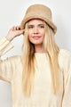 Model holding brim of tan faux fur bucket hat and wearing ivory sweater