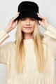 Model holding brim while wearing black faux fur bucket hat