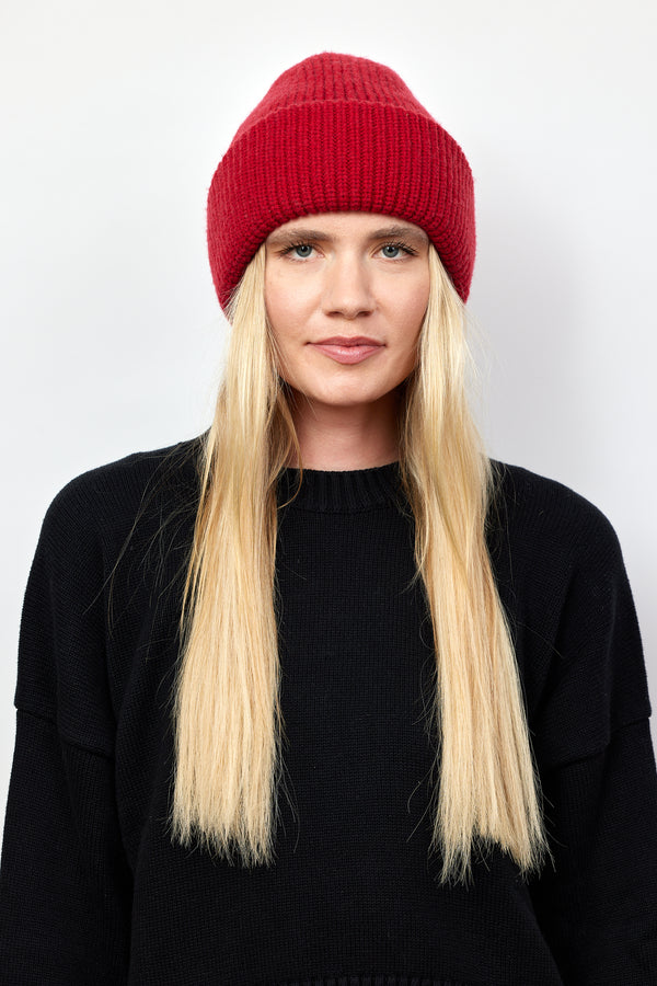 Model wearing red knit cuffed beanie and black sweater and looking at camera