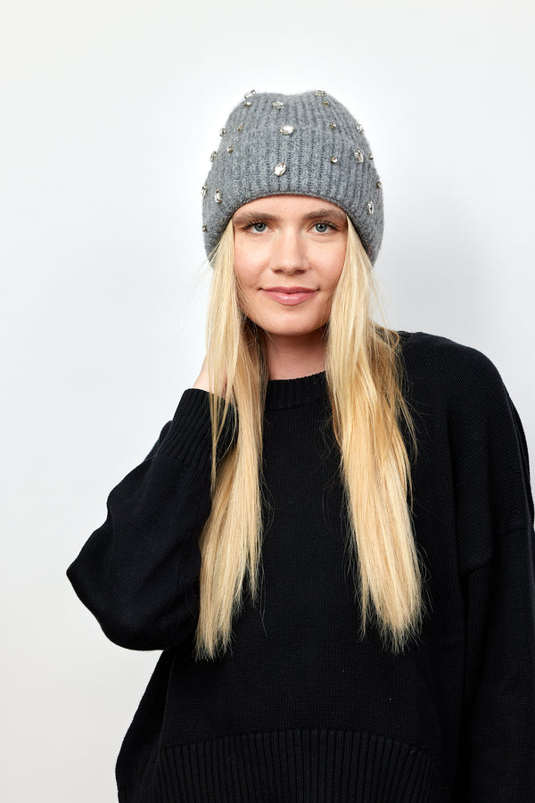 Model wearing black sweater and holding grey ribbed beanie with crystal embellishments