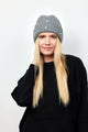 Model wearing black sweater and holding grey ribbed beanie with crystal embellishments