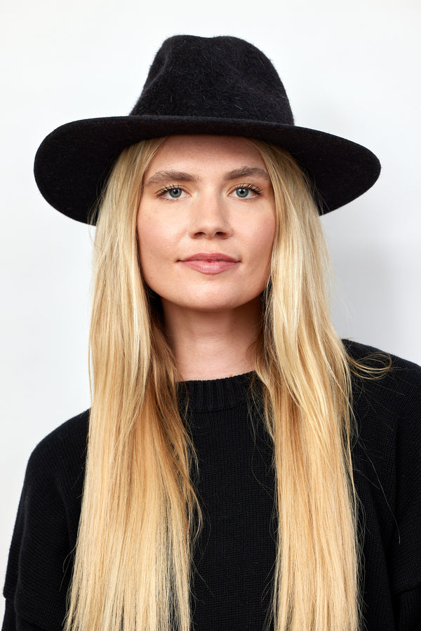 Model wearing black velour brimmed hat and black sweater