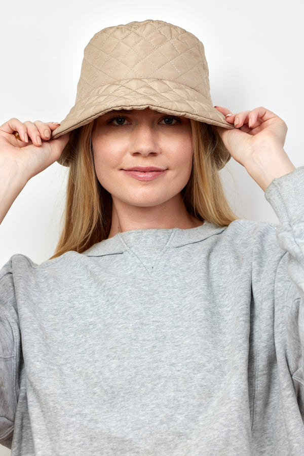 Model holding brim of tan quilted bucket hat