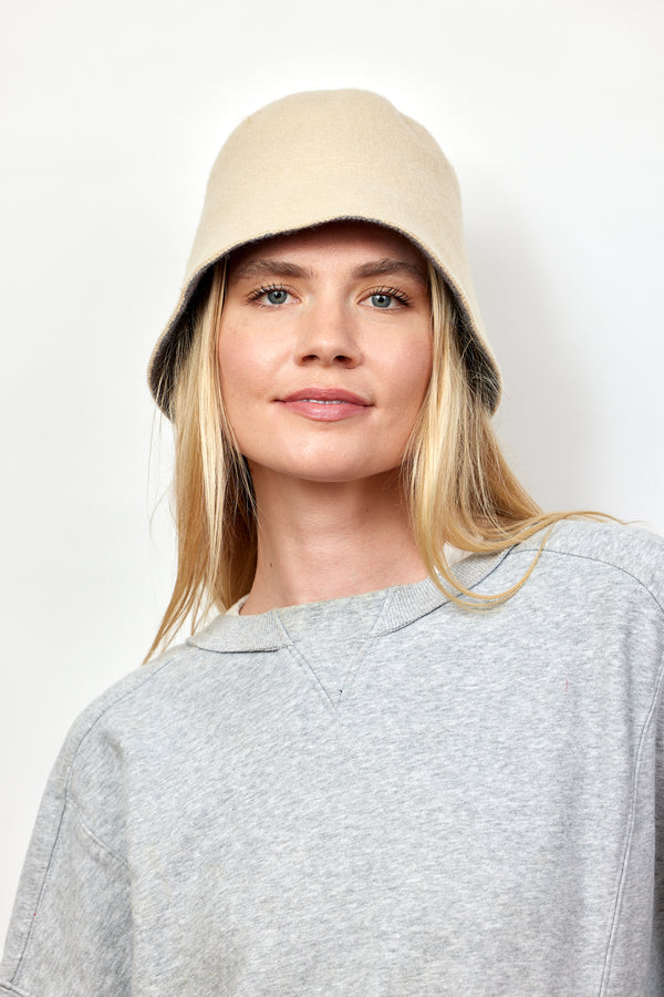 Model with blonde hair wearing tan knit bucket hat and grey sweatshirt