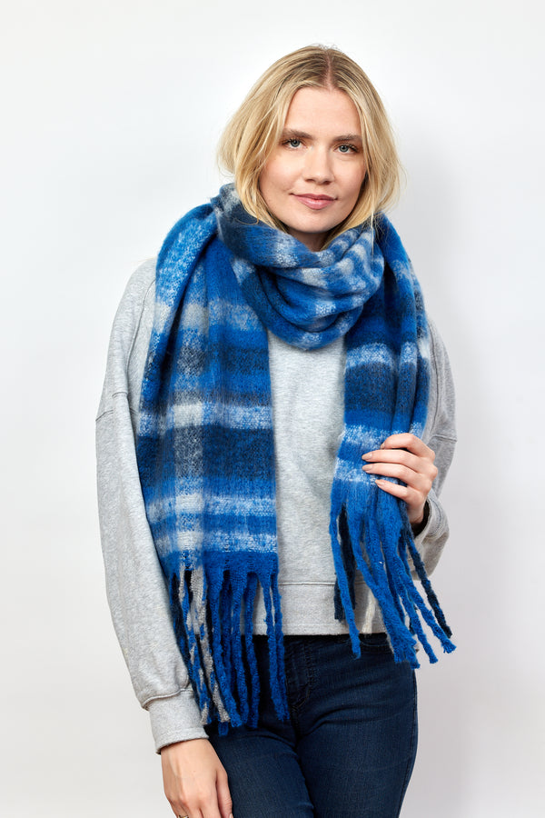 Model wearing blue and ivory plaid scarf with fringe detail