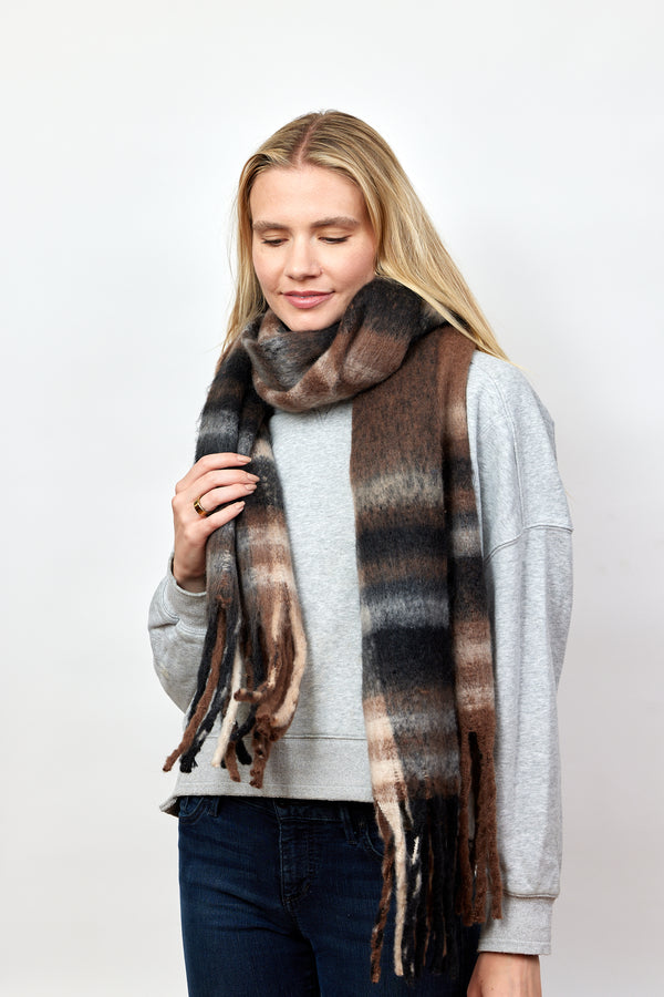 Black, brown and tan plaid scarf with fringe detail on model wearing jeans and sweatshirt