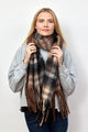 Model holding black, brown and tan plaid scarf with fringe detail around neck