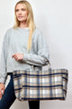 Model wearing grey sweatshirt and holding blue and brown plaid tote