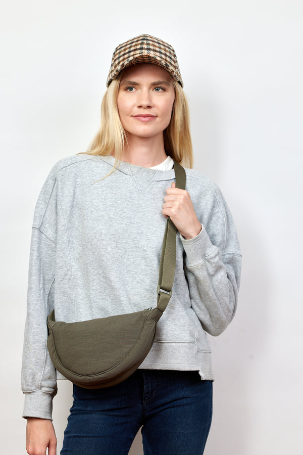 Model holding strap of olive nylon crossbody bag and wearing checkered baseball cap