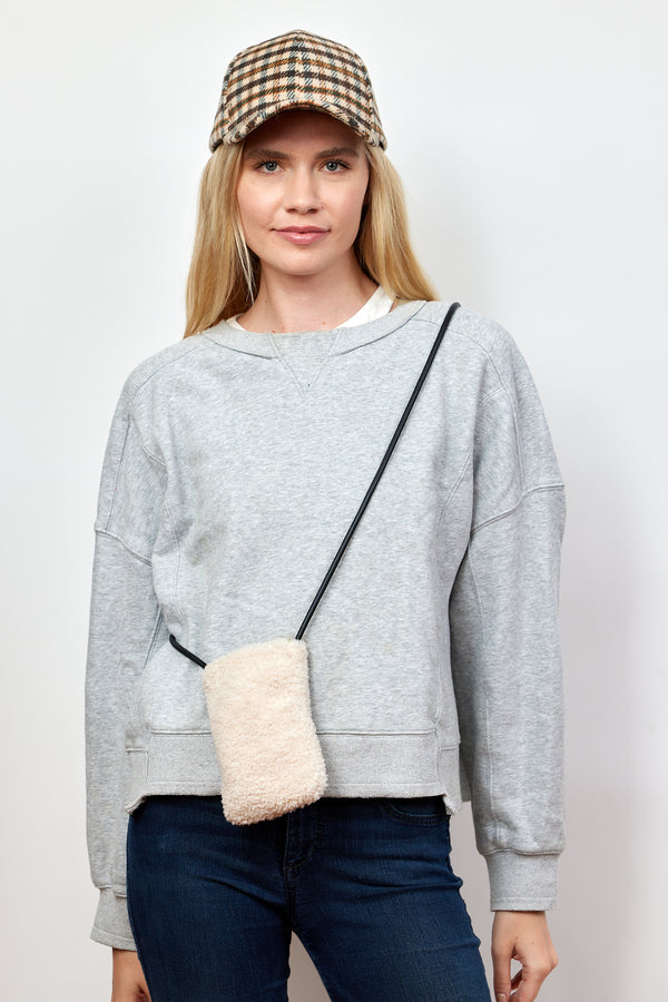 Model wearing ivory sherpa phone bag with crossbody strap and plaid baseball cap