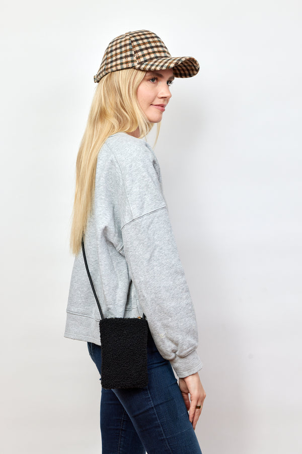 Model wearing black sherpa crossbody phone bag and plaid baseball cap