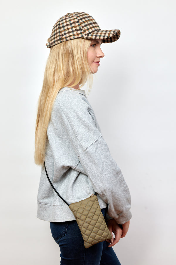 Model wearing olive quilted phone bag and baseball cap