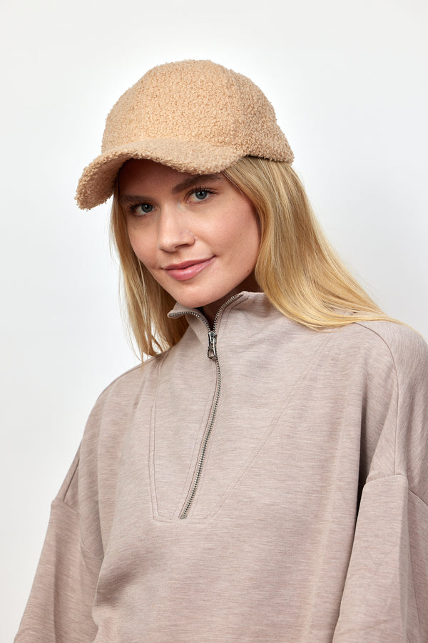 Model wearing light tan sherpa baseball cap and tan zip up sweatshirt