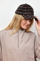 Model holding brim of dark plaid cap