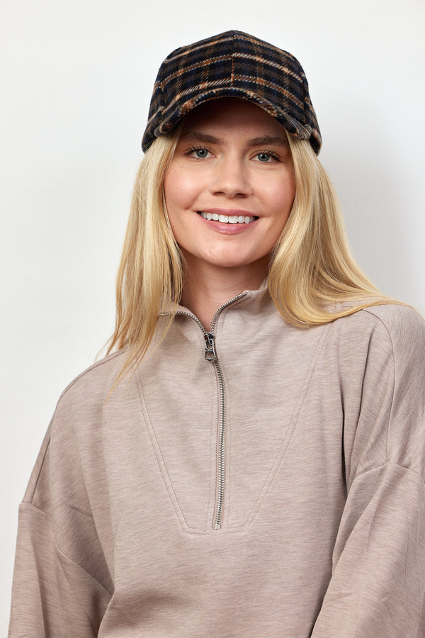 Model smiling and wearing dark plaid cap