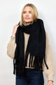 Model holding black solid scarf with fringe around neck