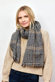 Model wearing black and tan herringbone scarf with tan sweater and dark jeans