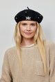 Model wearing black beret with crystal embellishments and tan sweater