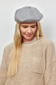 Model wearing grey beret with crystal embellishments and tan sweater