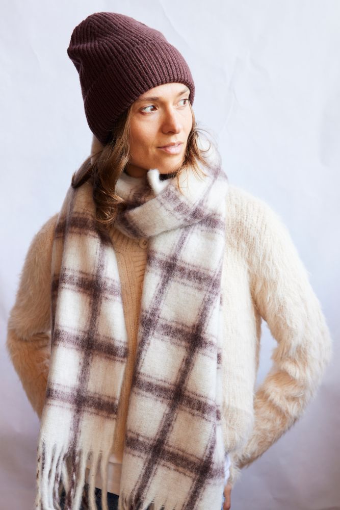 Person wearing a plaid scarf, beanie, and sweater against a light background