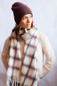 Person wearing a plaid scarf, beanie, and sweater against a light background