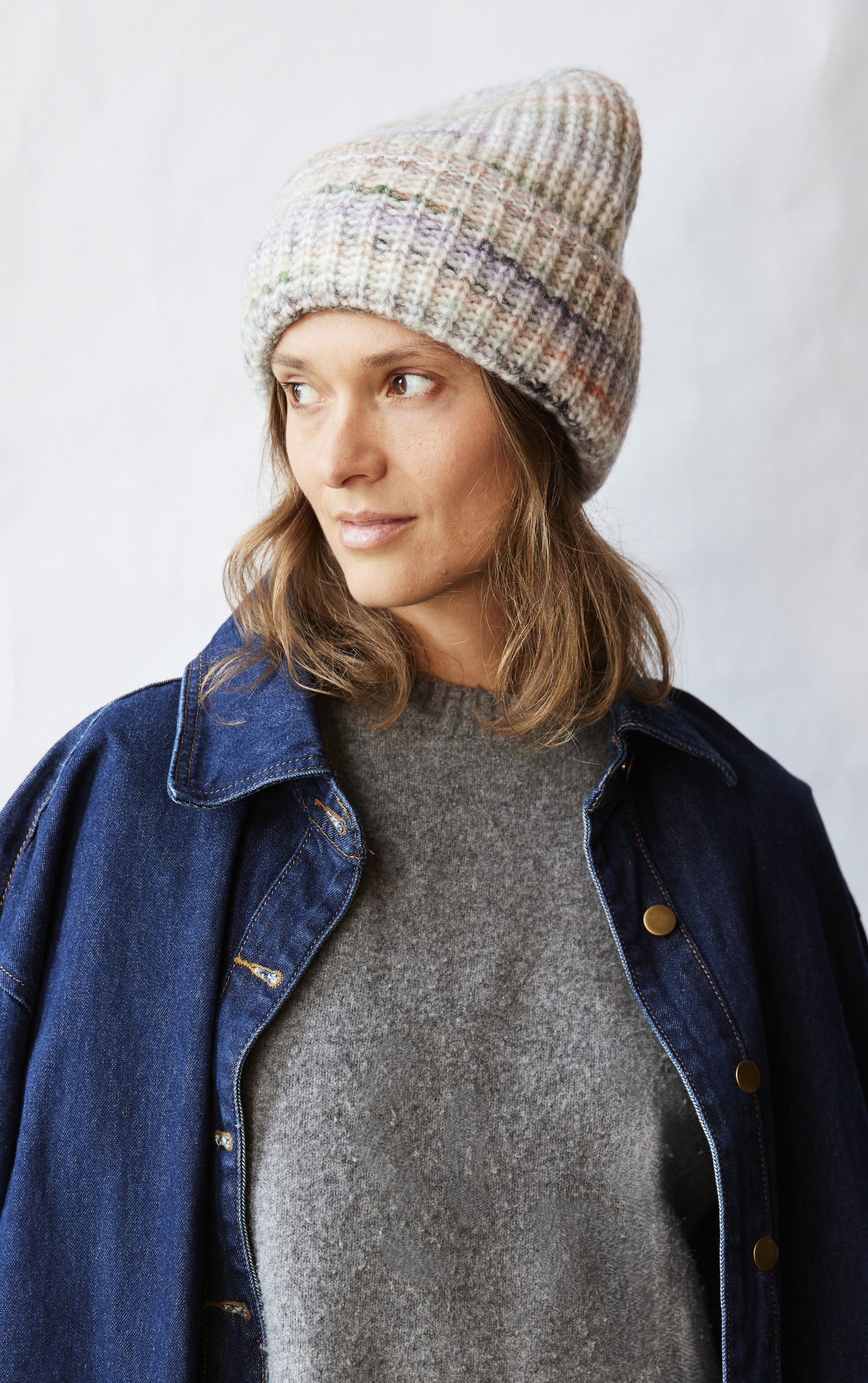 Woman wearing a knit beanie, gray sweater, and denim jacket against a white background